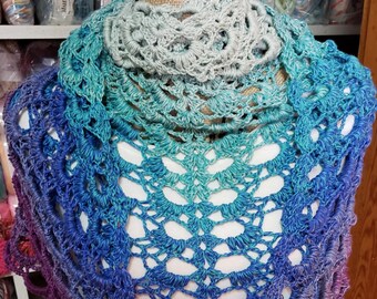 May include: A crocheted shawl with a gradient of colors from light blue to purple. The shawl is made with a delicate lace pattern and has a scalloped edge.
