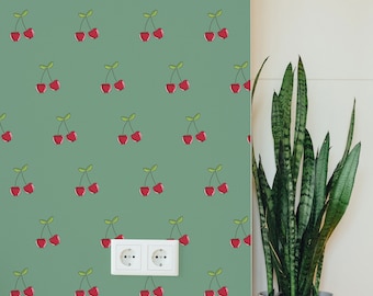 May include: A green wall with a repeating pattern of red cherries. The wall has a white electrical outlet with two plugs. A green plant in a white pot is in the corner of the image.