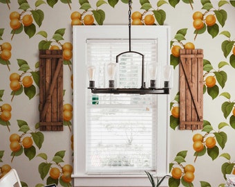 May include: A dining room with a wooden table and chairs, a laptop computer, two mugs, and a potted plant. The walls are covered in wallpaper with a pattern of orange fruit and green leaves.