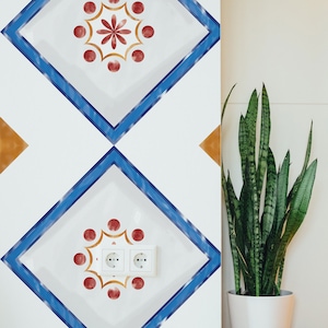 Puede incluir: Pared blanca con papel tapiz de patrón de diamante azul y naranja. Dos enchufes eléctricos son visibles en la esquina inferior derecha de la imagen. Una planta serpiente en maceta está en la esquina derecha de la imagen.