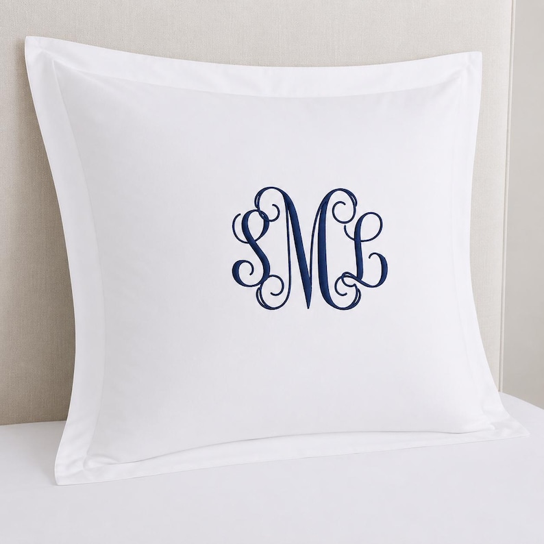 Puede incluir: Una funda de almohada cuadrada de color blanco con un borde ancho y un monograma bordado en azul marino centrado con las letras S, M y L en una fuente cursiva decorativa. La tela es de color blanco s&oacute;lido, lisa y con un acabado limpio.