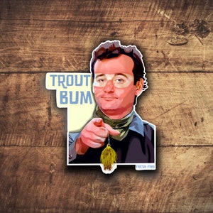 May include: A sticker featuring a cartoon illustration of Bill Murray with the text "Trout Bum" and a fishing lure. The sticker has a yellow background and a blue border.