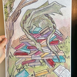 May include: A colored pencil drawing on paper depicting a green dragon curled up sleeping on a large stack of multi-colored books. A tree trunk is visible on the left side, and an open book lies on the ground in the lower right corner.