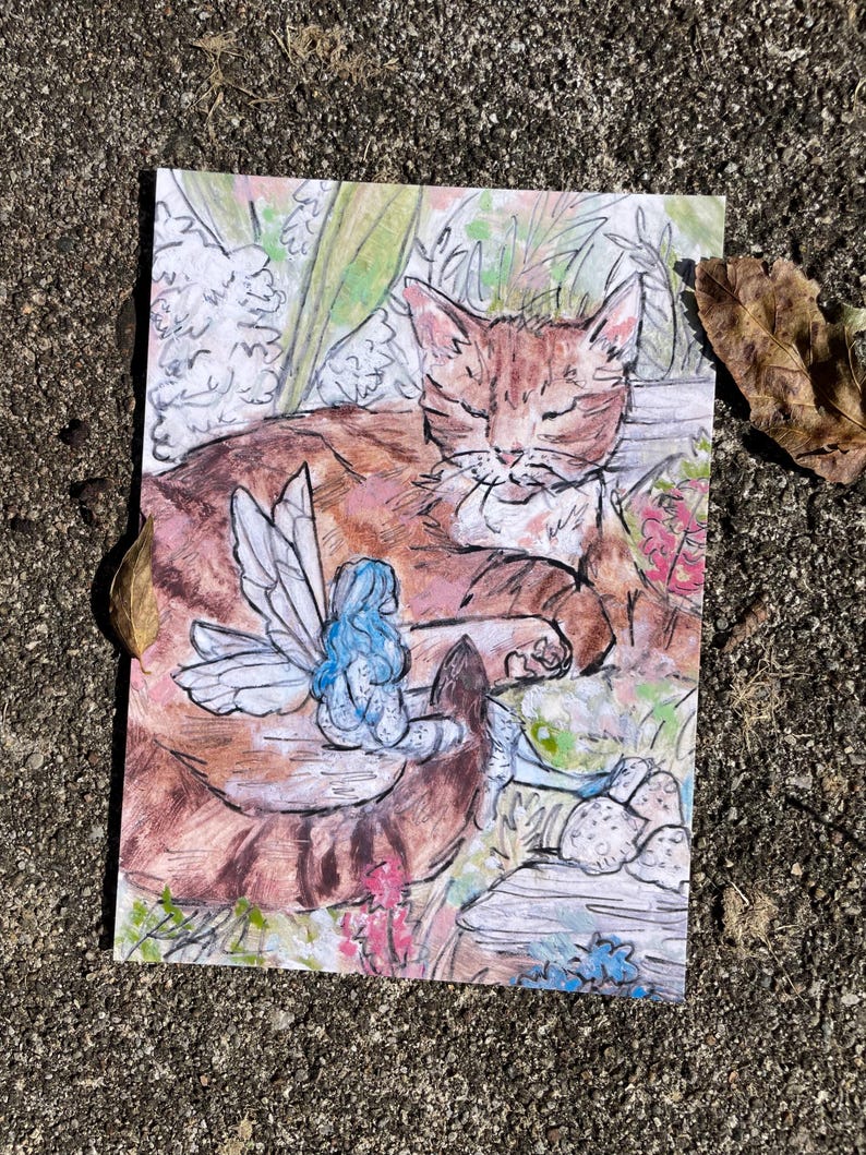 Puede incluir: Una ilustraci&oacute;n de acuarela de un gato atigrado naranja durmiendo con un hada azul con alas sentada en su espalda. El gato est&aacute; rodeado de follaje verde y flores rosas.
