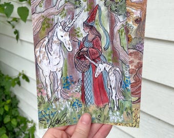 Peut inclure: Impression d'art à l'aquarelle représentant une femme en robe et chapeau rouges avec un panier, interagissant avec deux licornes dans une forêt. L'œuvre a un thème fantastique et fantaisiste avec des couleurs douces et des traits détaillés.