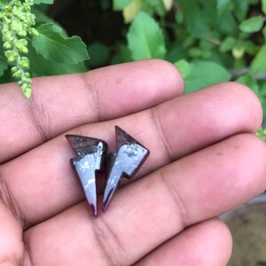 May include: A pair of small, black lightning bolt shaped earrings. The earrings are made of a shiny, metallic material.