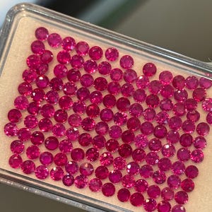 Könnte beinhalten: Eine Nahaufnahme eines Tabletts, das mit kleinen, runden, roten Edelsteinen gefüllt ist. Die Edelsteine sind in einem Gittermuster angeordnet und alle etwa gleich groß.
