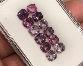 Può includere: Una collezione di otto pietre preziose sfaccettate, ottagonali, rosa e viola in una teca bianca.