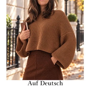 May include: A brown knit sweater with a wide, cropped silhouette and long, loose sleeves, paired with a dark brown skirt. The sweater features a textured garter stitch pattern, a round neckline, and a boxy fit that sits above the waistline.