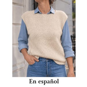May include: A sleeveless beige knit sweater vest worn over a light blue button-down shirt with long sleeves and blue denim jeans. The sweater vest features a round neckline and a simple stockinette stitch pattern, layered over a collared shirt.