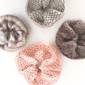 May include: Four knitted hair scrunchies in different colors and patterns. The scrunchies are brown and white, brown and black, beige, and pink.