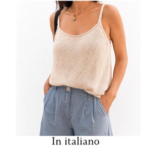 Può includere: Una canotta in maglia beige senza maniche con spalline sottili e scollo rotondo, abbinata a pantaloni in denim azzurro con chiusura a bottone singolo in vita e tasche laterali. Il top presenta una texture lavorata a maglia evidente.