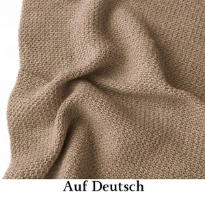May include: A light brown textile with a dense, uniform knit pattern featuring a textured surface. The fabric is draped in soft folds, creating subtle shadows and highlights across the material, which displays a consistent, neutral earth tone.
