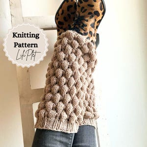 May include: Tan knitted leg warmers with a textured bubble stitch pattern. The leg warmers are shown over a pair of jeans and leopard print boots. The image includes the text "Knitting Pattern Lifi Plet".