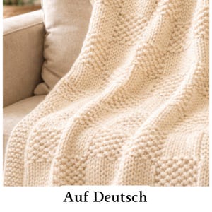 May include: A cream-coloured chunky knit throw blanket featuring a repeating textured pattern of alternating smooth stockinette stitch squares and bumpy seed stitch squares, creating a geometric grid design across the entire surface of the fabric.