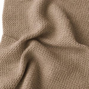 Könnte beinhalten: Ein hellbraunes Textil mit einem dichten, gleichmäßigen Strickmuster. Der Stoff weist ein konsistentes, kleinteiliges Texturgewebe auf, das eine Reihe weicher Falten und Schatten auf der Oberfläche erzeugt und die Tiefe des Materials betont.