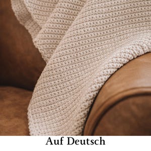 Può includere: Una coperta all'uncinetto color crema caratterizzata da un motivo a punti strutturato e coerente su tutto il tessuto. Il materiale presenta una trama densa e uniforme dall'aspetto morbido, che mette in risalto i nodi della lavorazione.