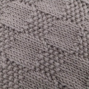 May include: Close-up of a gray knitted fabric with a textured pattern. The knit has a combination of raised and flat stitches, creating a visually interesting surface. The color is a muted, neutral gray.