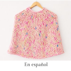 May include: A hand-knitted poncho featuring a chunky, textured stitch pattern in a variegated yarn blend. The garment displays a soft color palette of cream, bright pink, yellow, and blue flecks throughout the knit, hanging from a wooden hanger.
