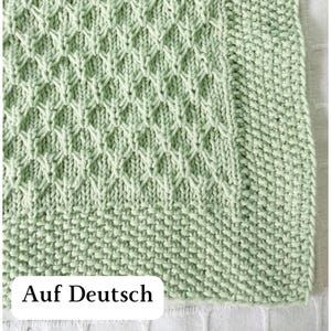 May include: Close-up of a light green knitted fabric with a diamond pattern. The bottom edge has a textured, ribbed design. The text "Auf Deutsch" is displayed on a white rectangle at the bottom.