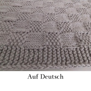 May include: A light gray knitted textile featuring a repeating geometric pattern of alternating squares. The fabric displays a textured surface created by a combination of stockinette and garter stitches, finished with a ribbed border edge.