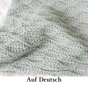 May include: A light sage green knitted blanket featuring a repeating textured wave pattern. The fabric displays a dense, consistent stitch construction with raised ridges that create a rhythmic, undulating visual effect across the entire surface.