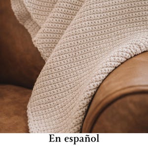 May include: A cream-colored crochet blanket featuring a dense, uniform stitch pattern. The textile has a thick, textured appearance with visible loops throughout the fabric, creating a consistent grid-like surface across the entire visible area.