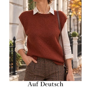 Può includere: Un gilet in maglia senza maniche color ruggine indossato sopra una camicia bianca a maniche lunghe con colletto, abbinato a pantaloni marroni a quadri. L'outfit include una tracolla di una borsa in pelle marrone visibile sul petto.