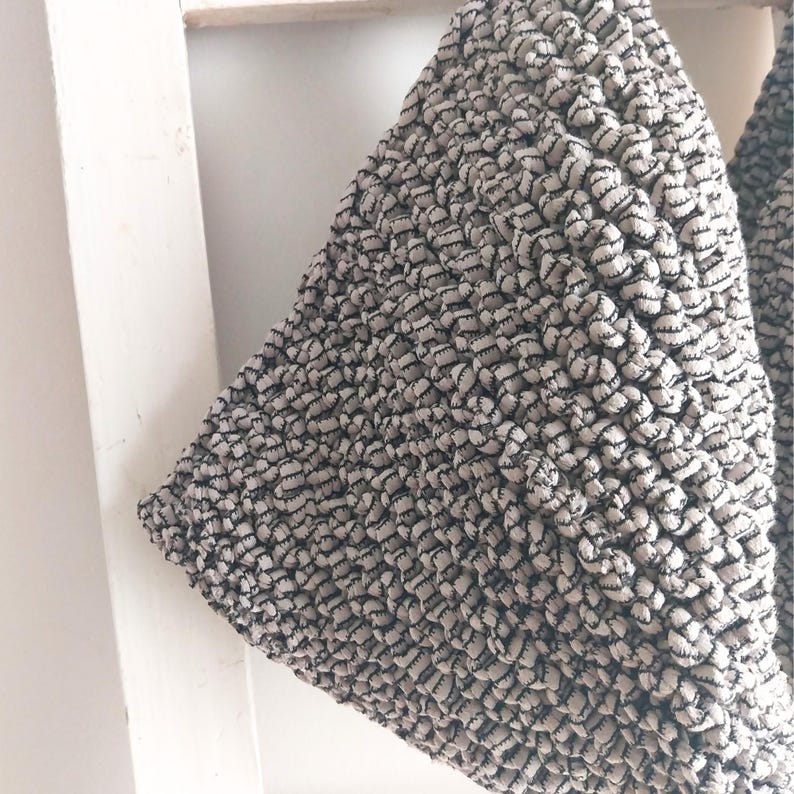 May include: A close-up of a beige and black crocheted tote bag. The bag is made of thick, textured yarn and has a simple, minimalist design.
