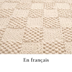May include: A cream-colored knitted textile featuring a repeating checkerboard pattern. The design alternates between squares of smooth stockinette stitch and squares of textured seed stitch, creating a tactile surface with a consistent light beige hue.