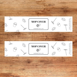 May include: Two white rectangular labels with the text "MOP COVER" and "HANDMADE WITH LOVE" in black. The labels have illustrations of cleaning supplies. The background is a wooden surface.