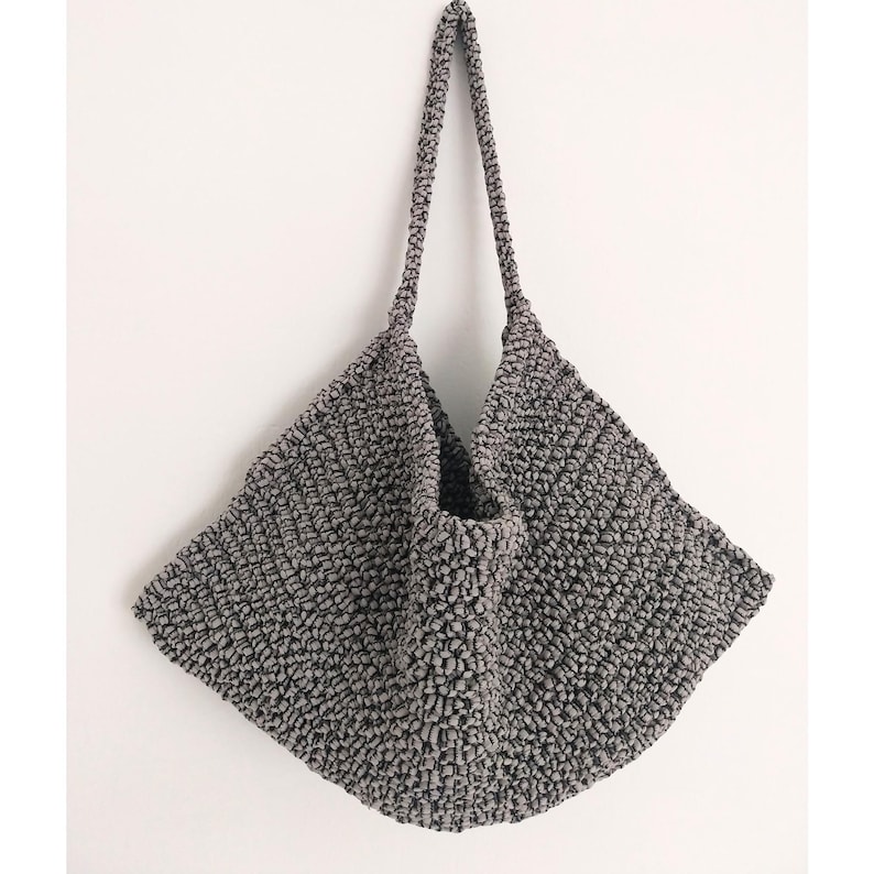 May include: A gray crocheted tote bag with a wide, flat base and two long straps.
