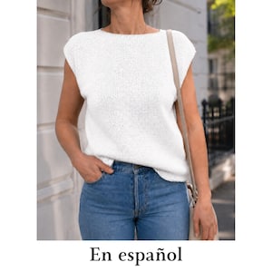 May include: A white sleeveless knit top with a boat neckline and a straight hem, paired with blue denim jeans. The top features a fine, uniform knit texture and a relaxed fit, while the jeans have a classic button-fly closure and a medium blue wash.