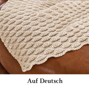 May include: A cream-colored crocheted blanket featuring a repeating textured leaf or petal pattern. The textile has a thick, yarn-based construction with a consistent stitch design throughout, creating a raised, dimensional surface across the fabric.