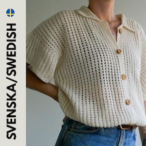 May include: Cream-colored, open-weave crochet shirt with a collared neckline and short sleeves. The shirt features wooden buttons down the front and is paired with blue denim jeans. The image has the text SVENSKA/SWEDISH.