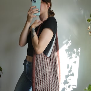 May include: A large, vertically striped tote bag in shades of brown and cream. The bag has a rounded bottom and a thick, solid brown border. The strap is also brown. The bag is being held over the shoulder.