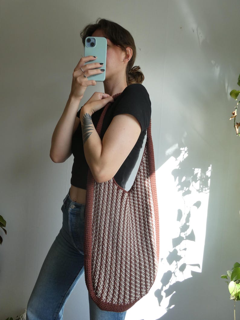 May include: A large, vertically striped tote bag in shades of brown and cream. The bag has a rounded bottom and a thick, solid brown border. The strap is also brown. The bag is being held over the shoulder.