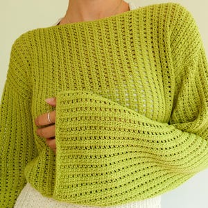 May include: A lime green crochet sweater with a loose fit and long sleeves. The sweater has a delicate open-stitch pattern.