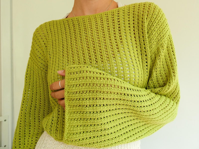 May include: A lime green crochet sweater with a loose fit and long sleeves. The sweater has a delicate open-stitch pattern.