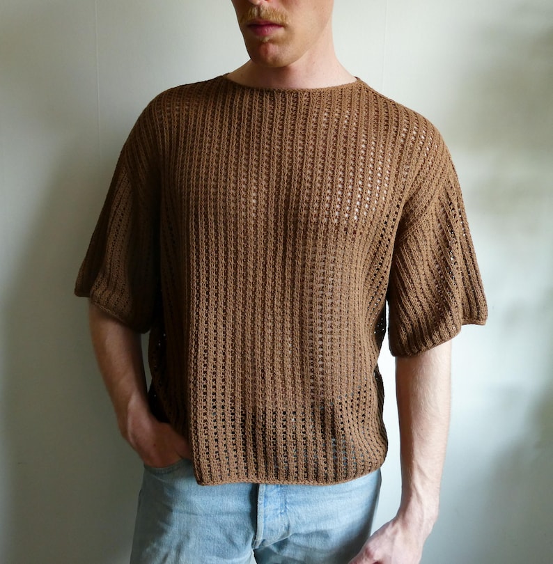May include: A brown, short-sleeved knit shirt with a textured, open weave design. The shirt has a crew neck and a relaxed fit. The color is a warm, earthy brown. The shirt is made of a lightweight material.