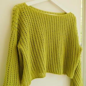 May include: A lime green crocheted sweater with a loose fit and a wide, open neckline. The sweater has a delicate, open-stitch pattern.
