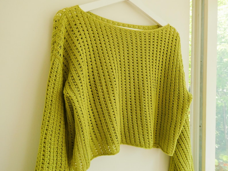 May include: A lime green crocheted sweater with a loose fit and a wide, open neckline. The sweater has a delicate, open-stitch pattern.