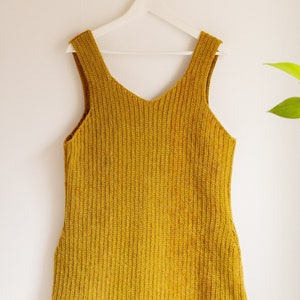 May include: A mustard yellow sleeveless knitted dress hanging on a white hanger.