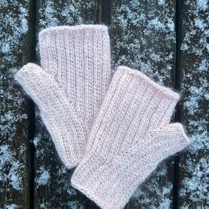 Könnte beinhalten: Ein Paar rosa gestrickte Fingerhandschuhe auf einer mit Schnee bedeckten Holzoberfläche.