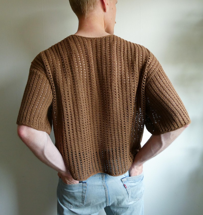 May include: A brown, short-sleeved crochet top with a ribbed design. The top has a relaxed fit and is made of a light brown yarn. The back of the top is visible, showing the texture and construction of the crochet.