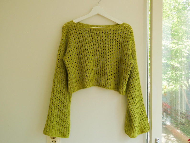 May include: A lime green crocheted sweater with long bell sleeves and a cropped fit.