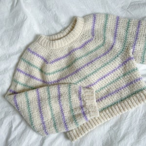 May include: A cream-colored sweater with purple and green stripes. The sweater has a crew neck and long sleeves.