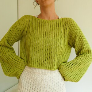 May include: A lime green knitted sweater with a loose fit and long sleeves. The sweater has a slightly cropped length and a delicate open-stitch pattern.