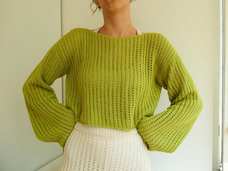 May include: A lime green knitted sweater with a loose fit and long sleeves. The sweater has a slightly cropped length and a delicate open-stitch pattern.