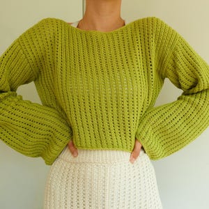 May include: A lime green knitted sweater with a loose fit and long sleeves. The sweater has a slightly cropped length and a delicate open-stitch pattern.